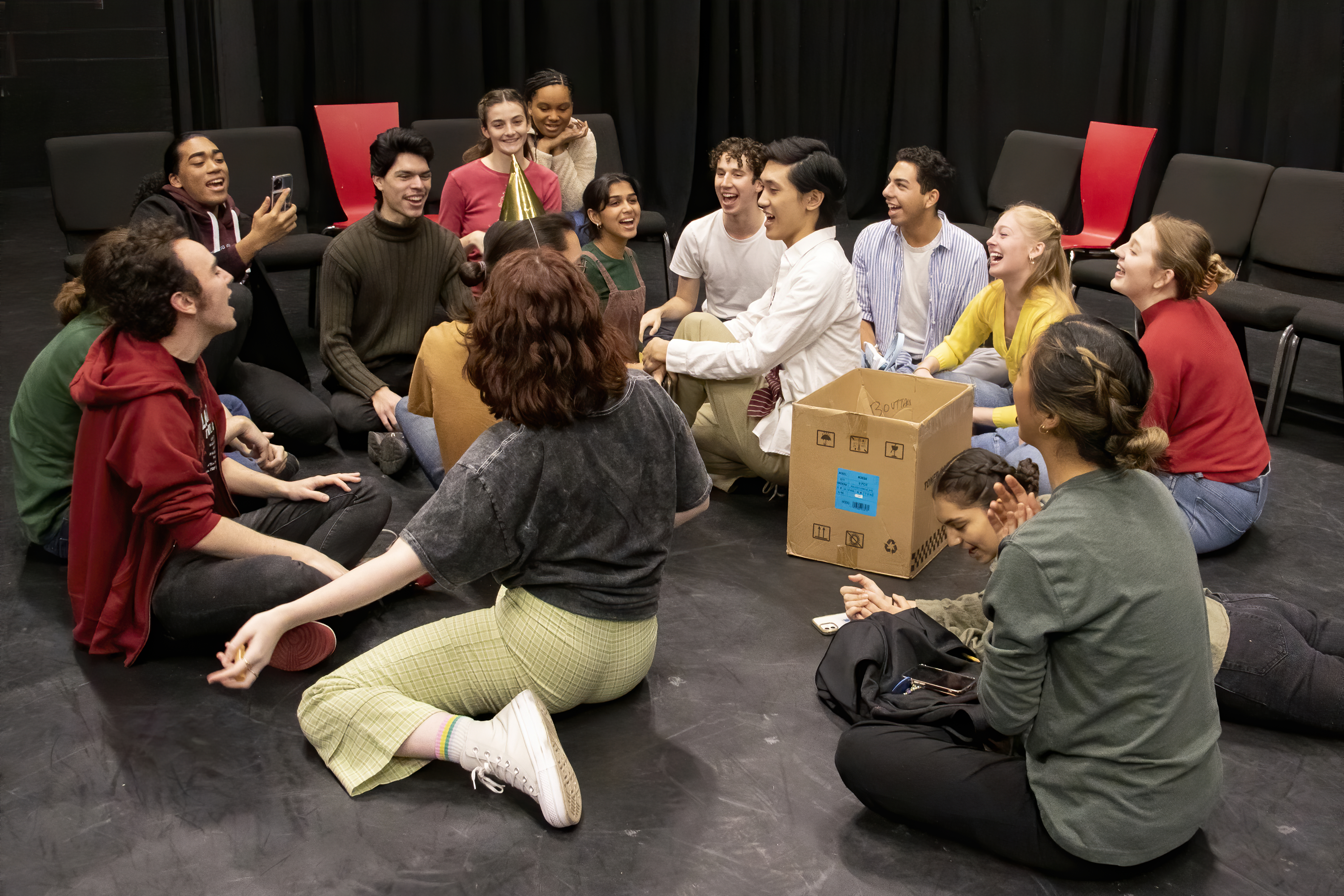 Fall 2022 students seated in a circle on the ground in a black box theatre